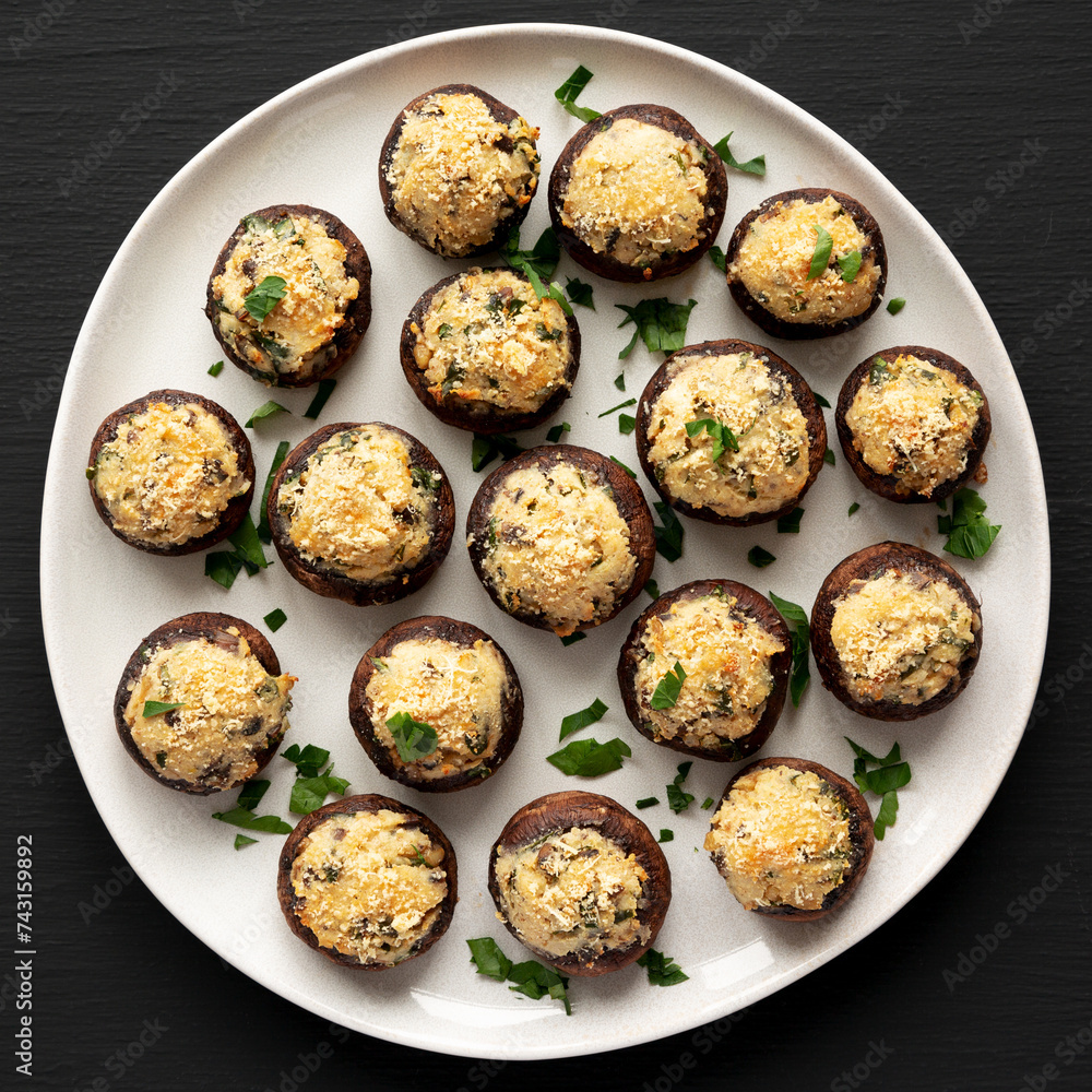 Homemade Garlic Parmesan-Stuffed Mushrooms on a plate on a black background, top view. Homemade Garlic Parmesan-Stuffed Mushrooms on a plate on a black background, top view.