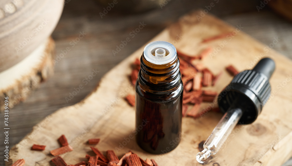A brown bottle of aromatherapy essential oil with red sandalwood chips