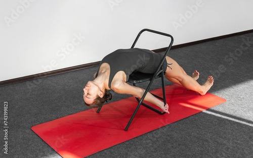 фотографія Yoga practitioner in sportswear, chair used as support to perform prasarita parsvakonasana pose
