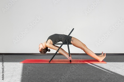 Yoga practitioner in sportswear, chair used as support to perform prasarita parsvakonasana pose.