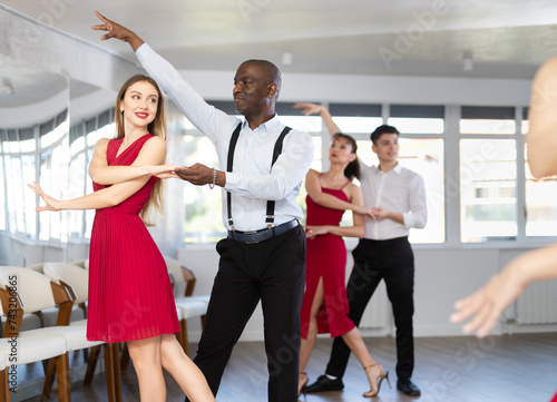 With unhurried music, African man and woman in couple spins to rhythm of waltz during lesson for novice students. Classes in mini-groups for those who want to learn dancing