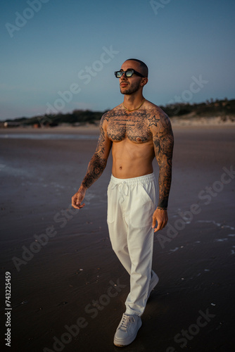Wallpaper Mural Chico joven tatuado y musculoso posando sin camiseta en la playa al atardecer Torontodigital.ca