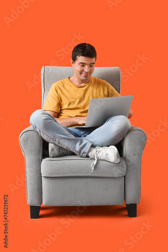 Young man using laptop in armchair on red background © Pixel-Shot