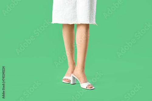 Legs of young woman in stylish white sandals on green background