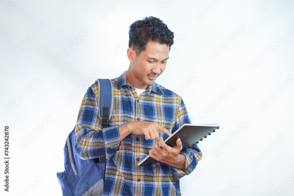 Smiling happy young Asian man student wearing shirt with backpack glasses pointing finger at book isolated on white background. Education in high school university college concept Smiling happy young Asian man student wearing shirt with backpack glasses pointing finger at book isolated on white background. Education in high school university college concept