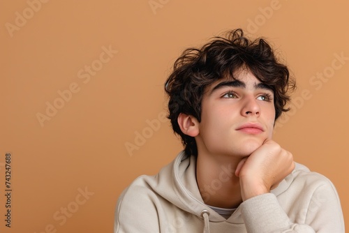 A bored teenage boy with his hand on his chin, looking away in deep thought.