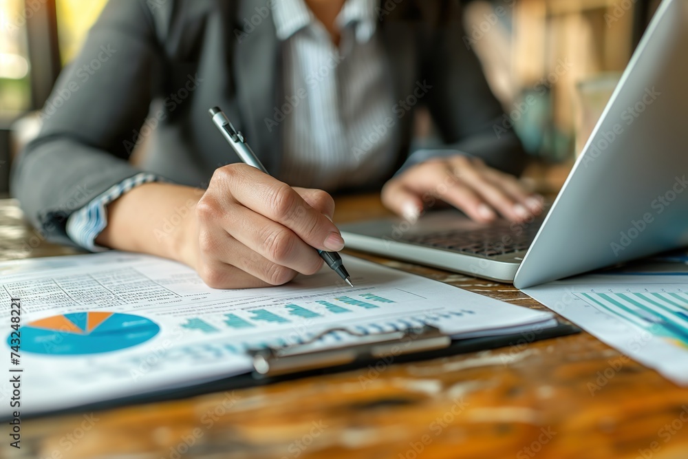A woman sitting at a table, working on a laptop and using a pen to take notes. A woman sitting at a table, working on a laptop and using a pen to take notes.