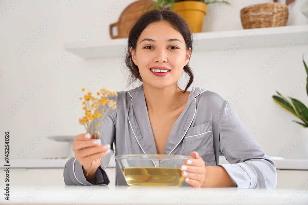 Young Asian woman preparing steam inhalation with herbs at table in kitchen