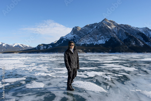 person standing on frozen lake in front of mountain on clear blue sky sunny day