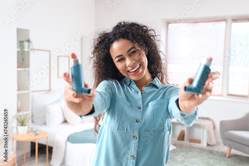 Smiling young African-American woman with asthma inhalers in bedroom photo