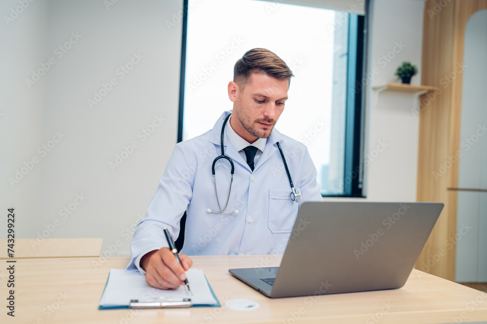 Male Doctor expert wearing white coat using laptop and reading clipboard report at work in hospital. Male Doctor expert wearing white coat using laptop and reading clipboard report at work in hospital.