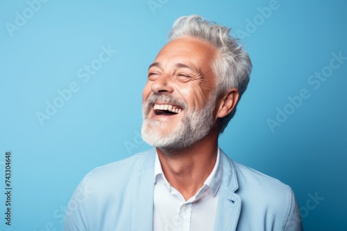 Cheerful senior man is laughing and looking at camera. Isolated on blue background