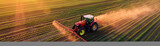 Aerial view of a tractor spraying pesticide on the field at sunset.