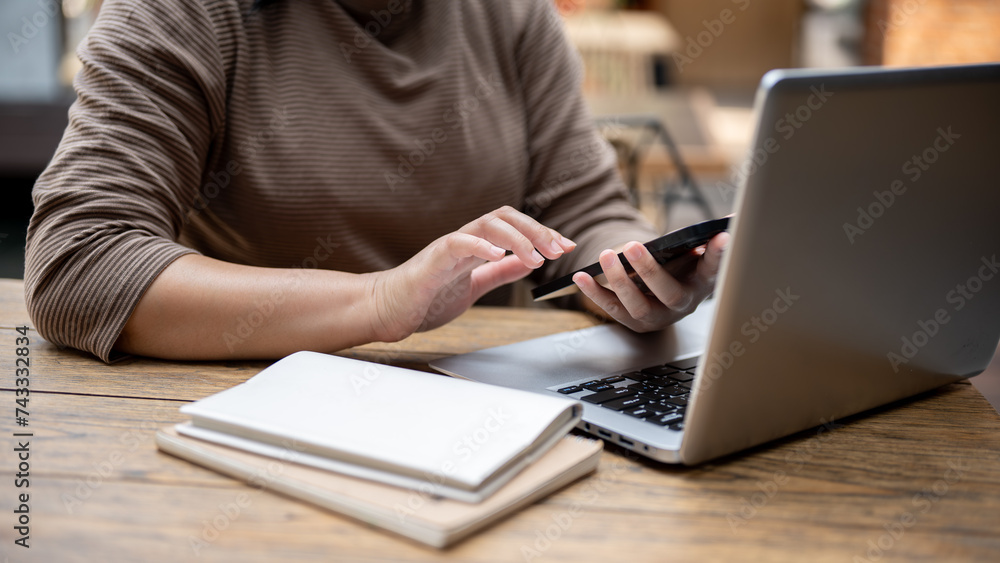 Naklejka premium A cropped shot of a woman working remotely at a coffee shop, using her smartphone at a table.