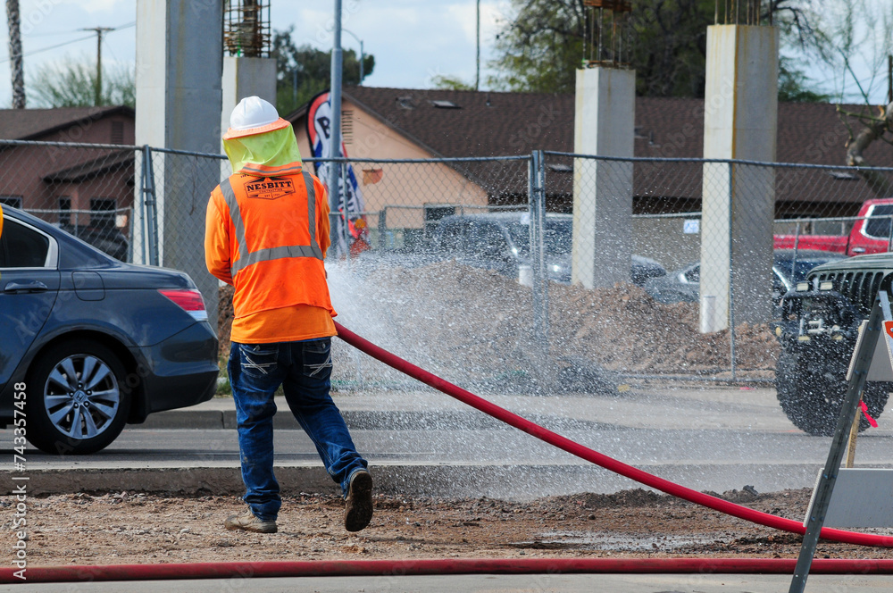 A construction worker sprays water with an industrial orange hose for ...