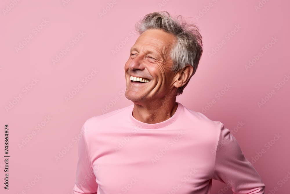 Portrait of a happy senior man with grey hair laughing and looking at camera against pink background