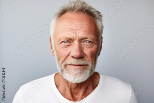 Portrait of a senior man with grey hair and beard looking at camera against grey background