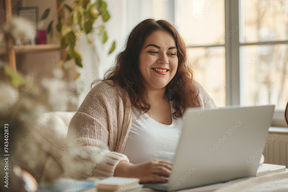 beautiful plus sized brunette woman working from home, sitting and using laptop, smiling and looking to the screen, video call. beautiful plus sized brunette woman working from home, sitting and using laptop, smiling and looking to the screen, video call.