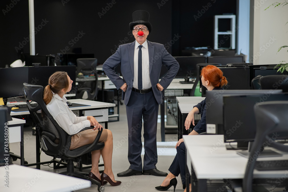 Two Caucasian women sitting in the office and looking at a clown. Two Caucasian women sitting in the office and looking at a clown.