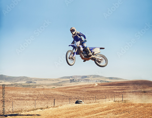Person, jump and dirt bike of professional motorcyclist in the air for trick, stunt or race on outdoor track. Expert rider on motorbike or scrambler in dunes or extreme sport with blue sky mockup