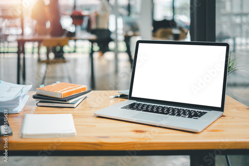 An organized work setup featuring a laptop with a blank screen, notebooks, and a plant on a wooden table in a bright office.