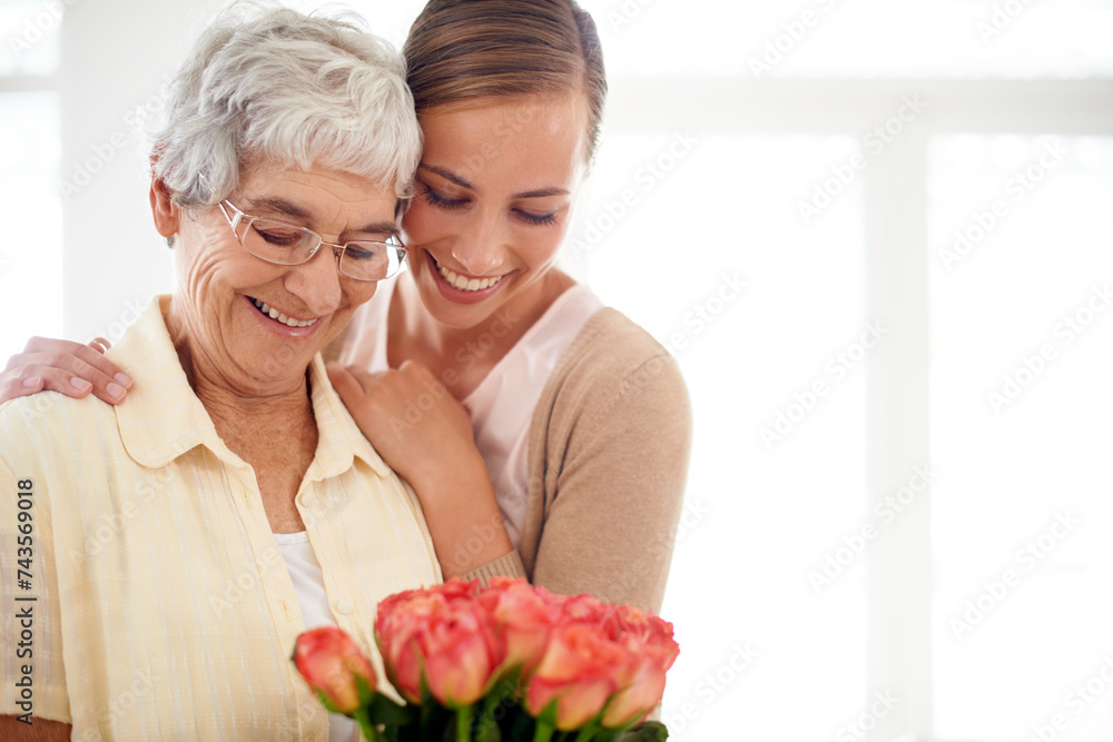 Senior woman, daughter and hug with flowers, present and care for love, bonding or reunion at family home. People, elderly mom and mothers day celebration for connection, gift or bouquet in apartment Senior woman, daughter and hug with flowers, present and care for love, bonding or reunion at family home. People, elderly mom and mothers day celebration for connection, gift or bouquet in apartment