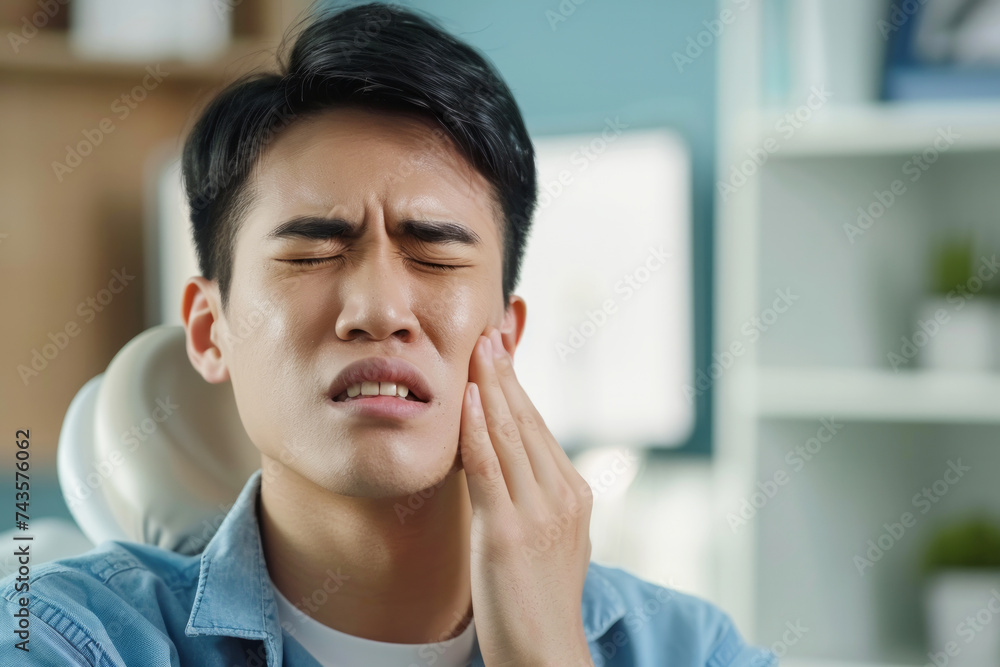 Asian Man Experiencing Severe Toothache Pain Touching Jaw. Man with toothache. Dentistry and dental care. Painful view of asian man. He groans in pain. man closes his eyes and grimaces in pain.