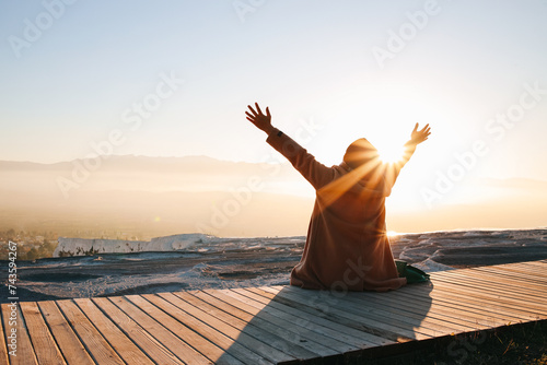 Rear view of woman sitting alone enjoying the sunrise with open arms