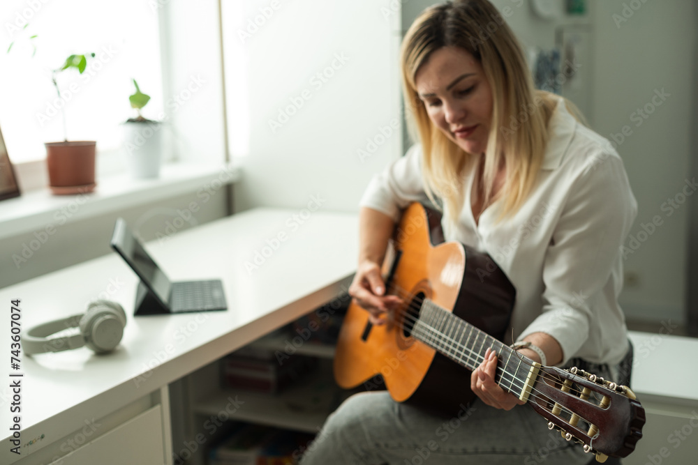 Home Guitar Playing Lesson Girl Hold Instrument. Beautiful Woman at Musical Training. Blonde with Makeup Looking at Notes on Music Stand. Caucasian Girl Guitarist Taking Chords on Strings