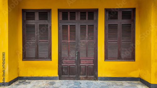 Traditional dark brown wooden door and window shutters on a vibrant yellow wall, with copy space for text, suitable for backgrounds on architecture and design themes