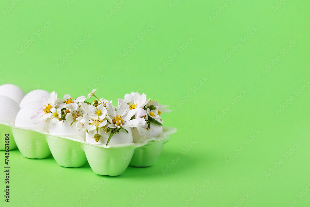 White eggs in egg tray with spring pear and strawberry flowers on a green background. Happy Easter