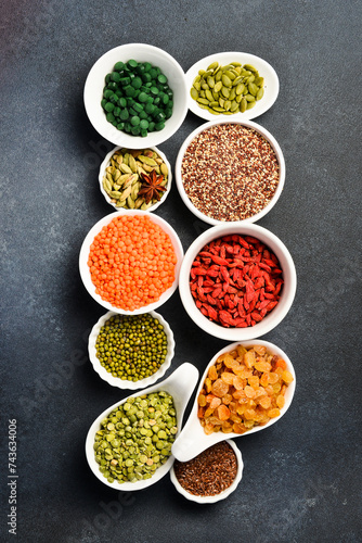 Set of superfoods, cereals, nuts and dried fruits, spirulina and goji in white ceramic bowls. On a gray concrete background. Top view. Free space for text.