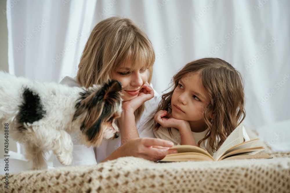 Book, dog, reading together. Mother with daughter are at home Book, dog, reading together. Mother with daughter are at home