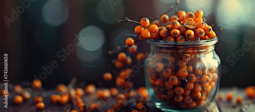 A glass jar sits on a wooden table, filled with ripe orange sea buckthorn berries. The vibrant berries stand out against the warm tones of the wood.