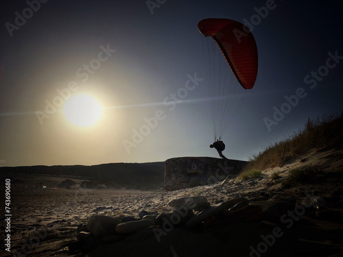 backlit sun silhouette of a man paragliding on the beach of a man jumping on the beach