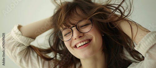 A happy woman with long brunette hair is standing outdoors, feeling the wind in her hair. She is creating eyeglasses with her hands and exuding feminine beauty. photo