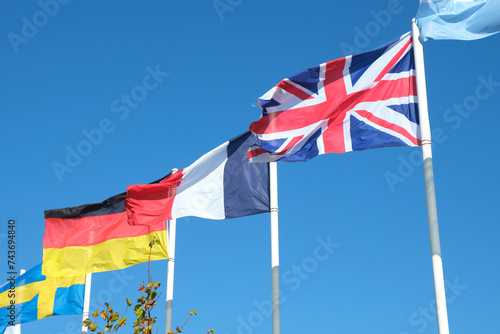 Group of flags waving . International relation between France , Germany and Great Britain and other countries . Blue sky background .