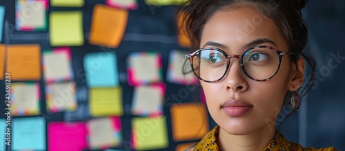 A young woman wearing stylish glasses is using stickers to develop a work project strategy in a brainstorming session while also presenting an idea for a startup.