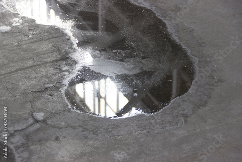 A puddle on the concrete floor reflects the ceiling with windows