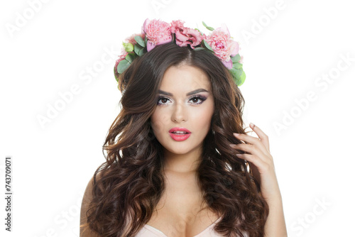 Elegant woman with make-up, perfect fresh skin and summer season rose flower wreath on her long healthy curly hairstyle looking at camera isolated on white background, studio portrait