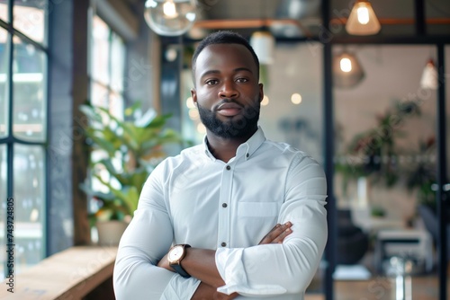 Confident black CEO male standing arms crossed in a modern office looking at camera. 