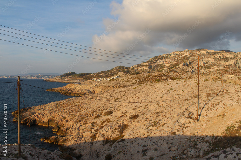 Wooden electric pylon and electric wires in the Calanques of Marseille, Les Goudes, France. Limestone rocks. Beautiful panorama with a cloudy evening sky.