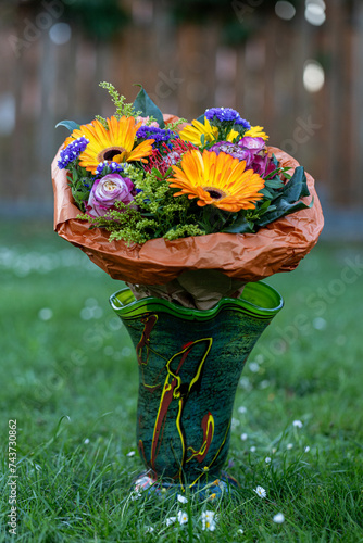 Gorgeous Birthday bouquet featuring orange Gerberas, pink Roses, pink and yellow Carnations. bouquet photographed in a green vase outside in the grass