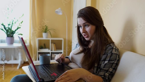 Smiling Caucasian woman working remotely on laptop sitting on couch, chatting online. The concept of remote work, online shopping, online work, happy family, digital lifestyle, online conference.