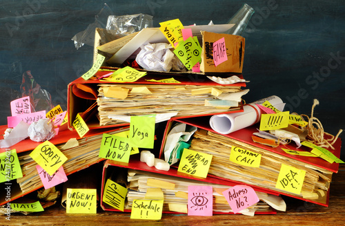Messy file folder,sticky notes and old papers on a cluttered , chaotic office desk. Red tape, bureaucracy,overworked,burnout,messy office and chaotic business concept.
