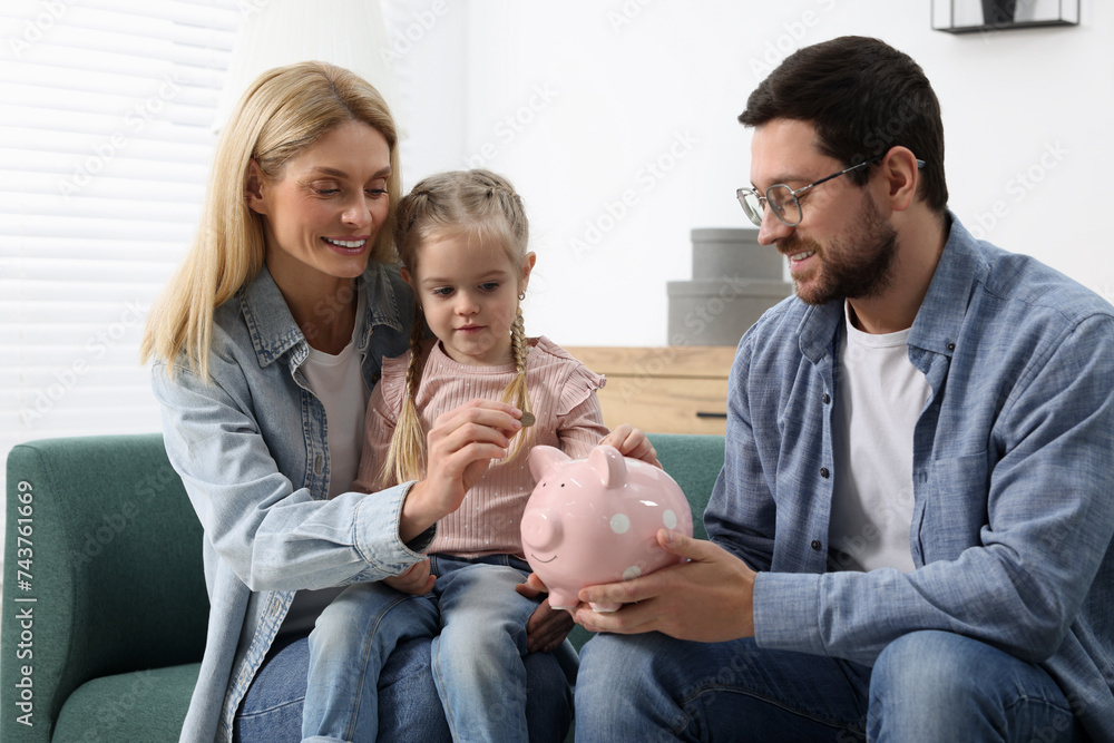 Planning budget together. Little girl with her parents putting coins into piggybank at home Planning budget together. Little girl with her parents putting coins into piggybank at home