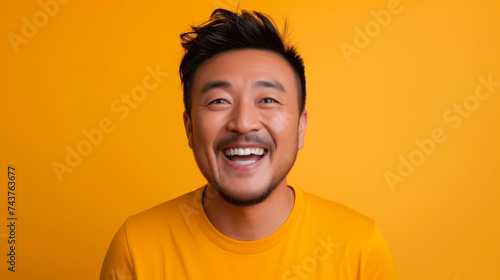 Asian guy portrait smiling to camera over yellowish background and empty space for text. © Elena Uve