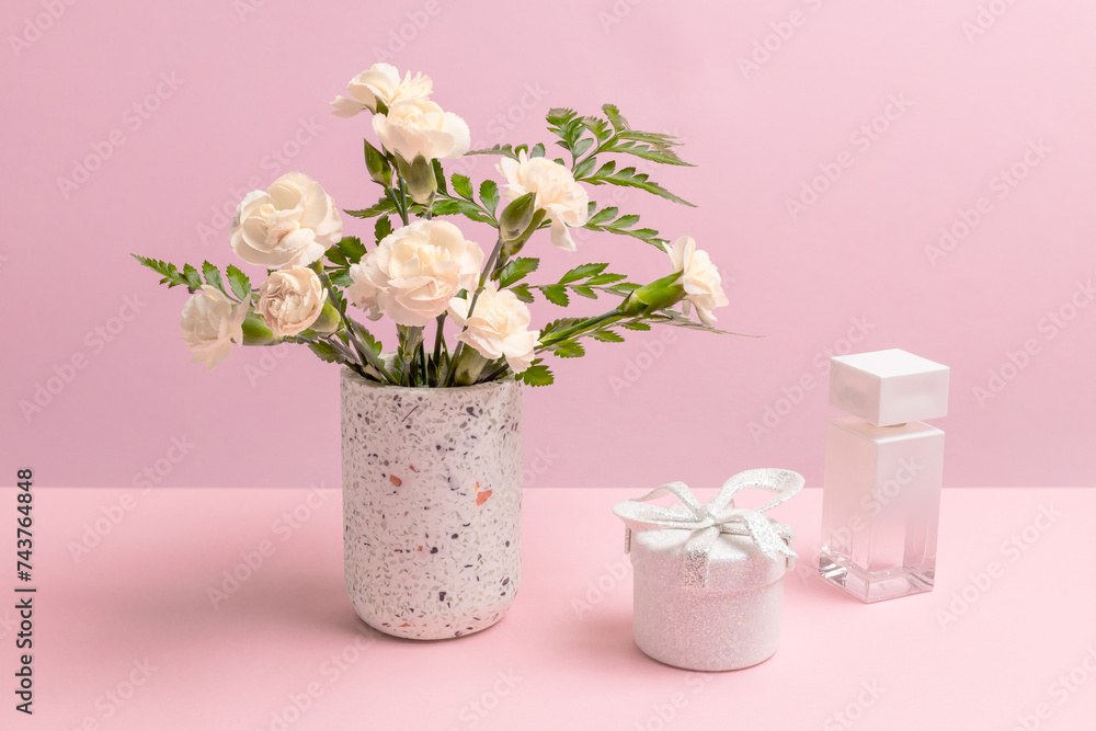 Bouquet of carnations in a vase with a gift box and a perfume.
