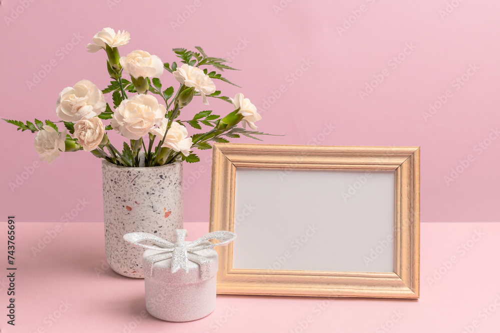 Bouquet of carnations in a vase with a gift box and a photo frame.