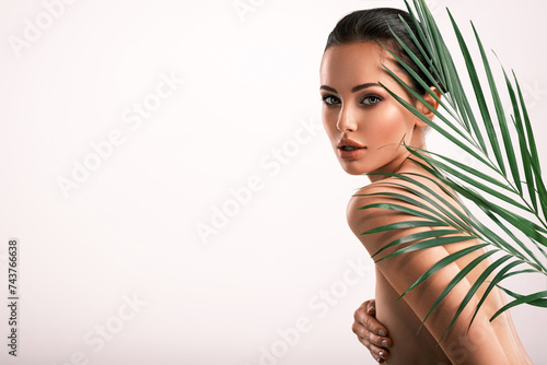 Young beautiful woman with green leaves near naked body. Body care beauty treatments concept.  Girl's  face with green flowers.